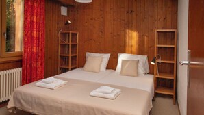 A wooden-paneled room with a bed, a radiator, a window with red curtains, and a bookshelf.