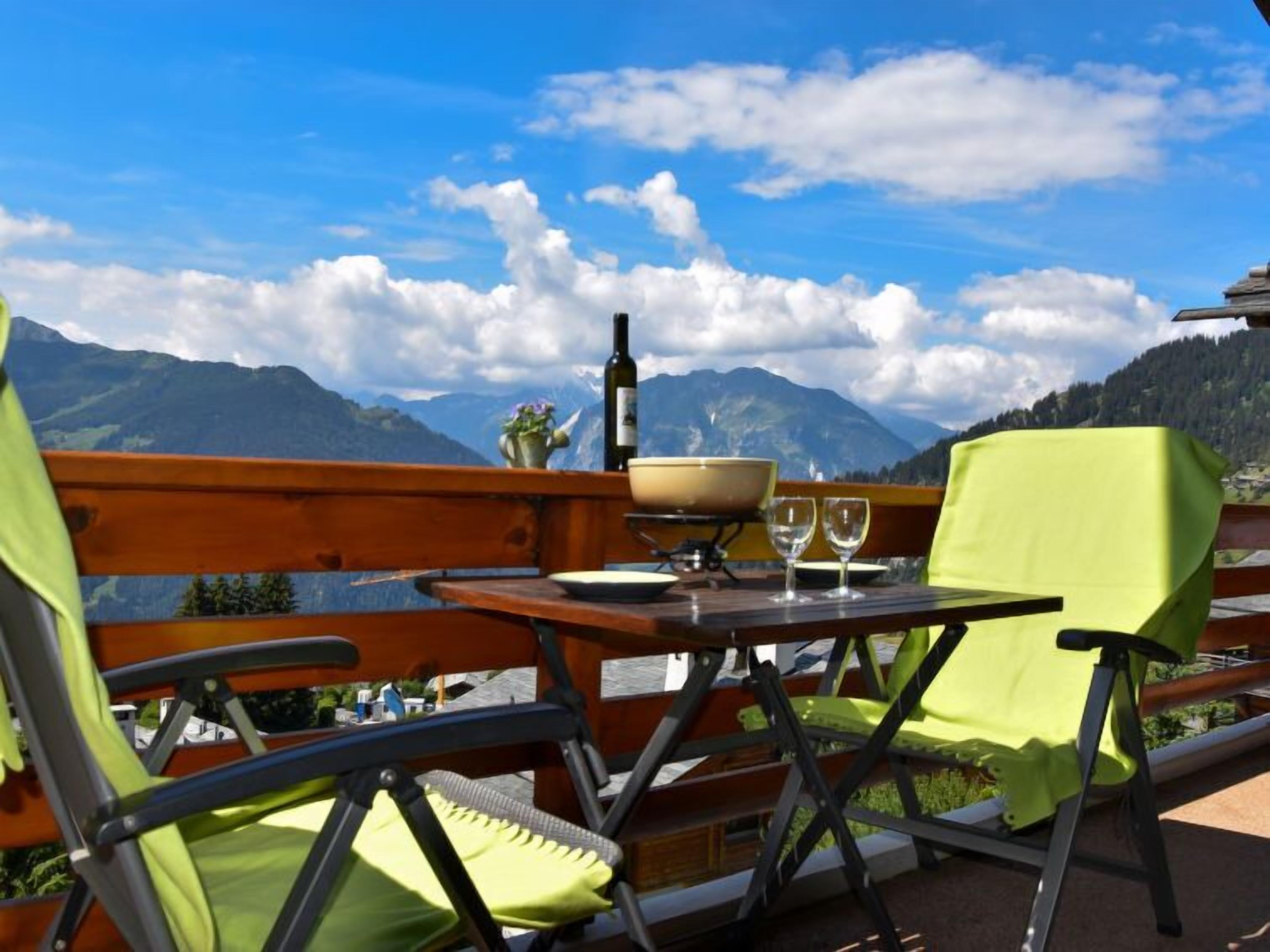 A balcony with a table set for two, overlooking a mountainous landscape.