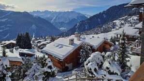 A snow-covered mountain village with wooden cabins and a view of distant mountains.