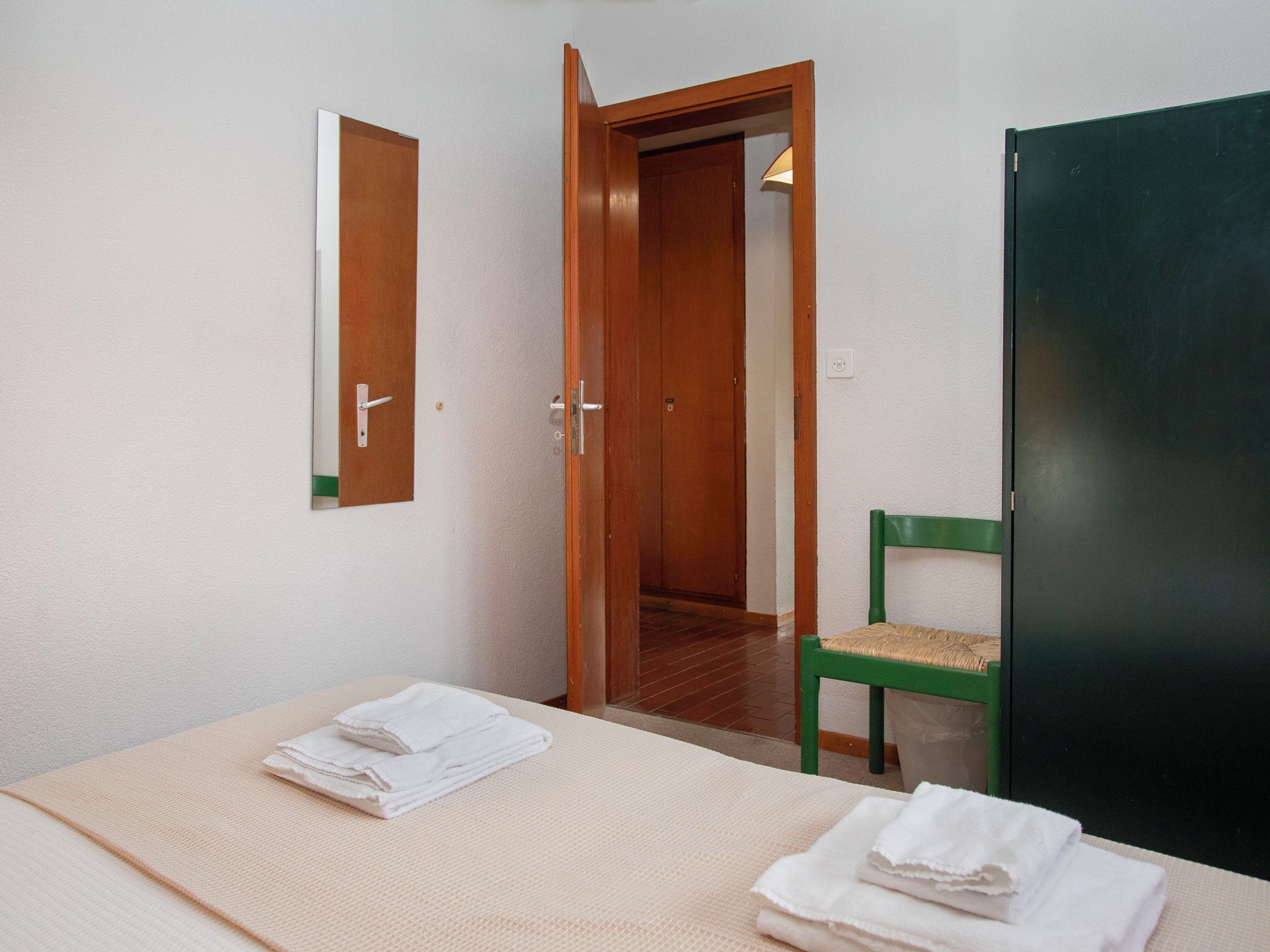 A room with a bed, a chair, a mirror, and a door leading to another room.
