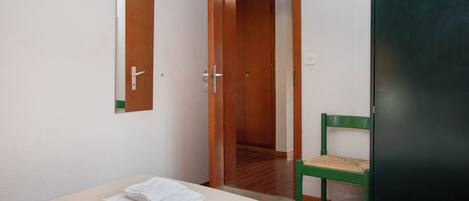 A room with a bed, a chair, a mirror, and a door leading to another room.