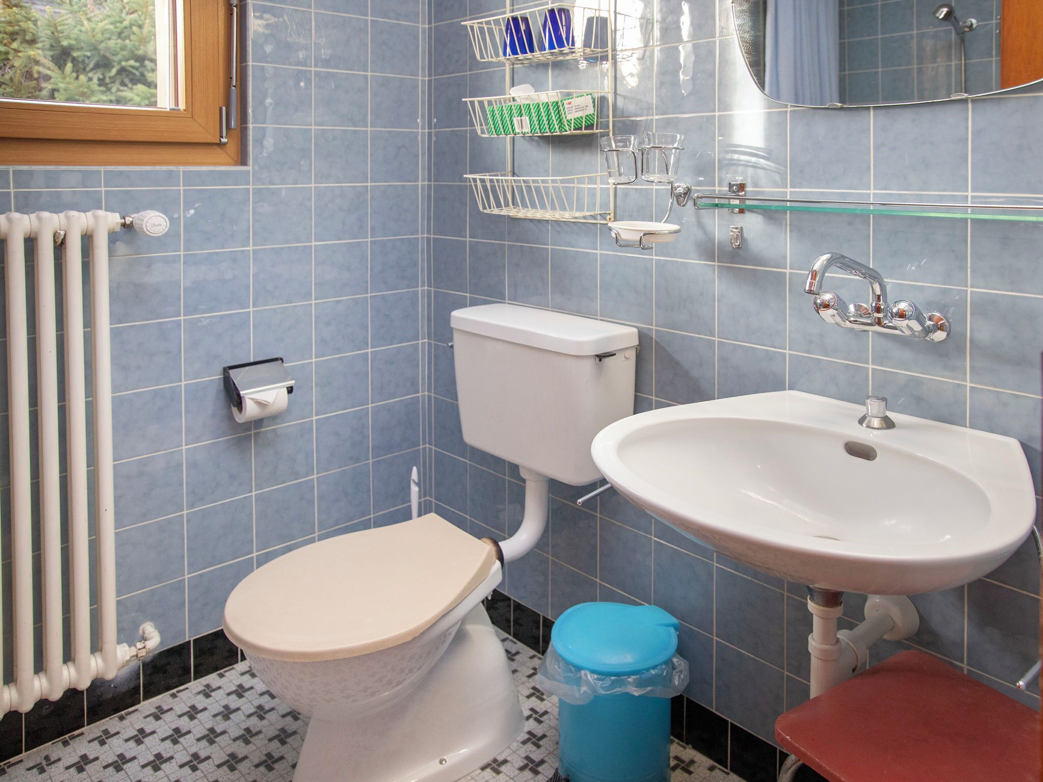 Un baño con inodoro, lavamanos y un cubo de basura azul.