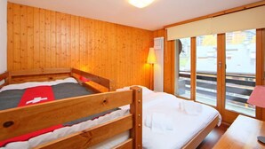 Een kamer met houten lambrisering, twee bedden, een raam met uitzicht op een gebouw en een tafel met een lamp.
