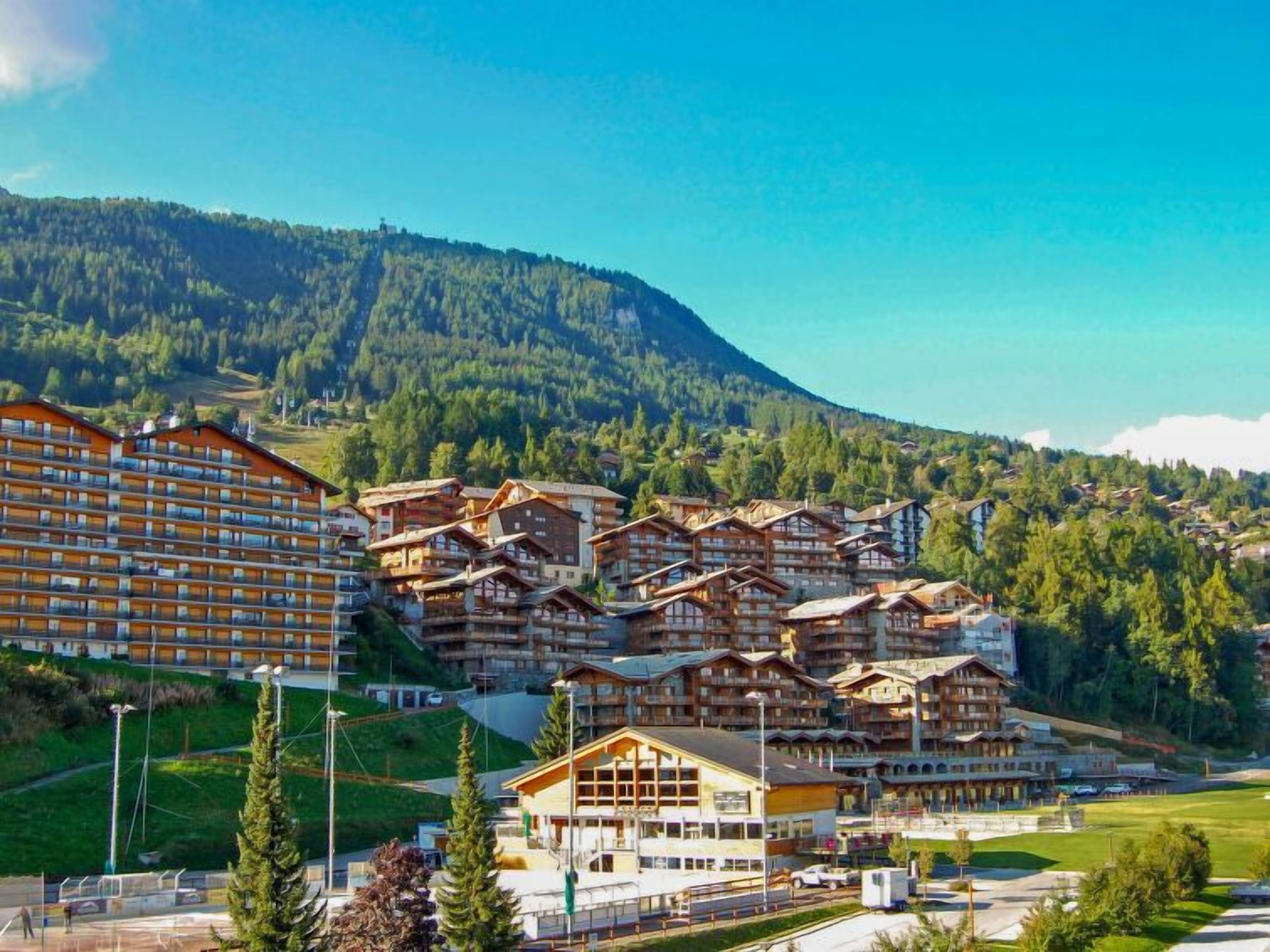 Un complejo turístico en la montaña con varias edificaciones tipo chalet, un hotel grande y una pista de esquí al fondo.