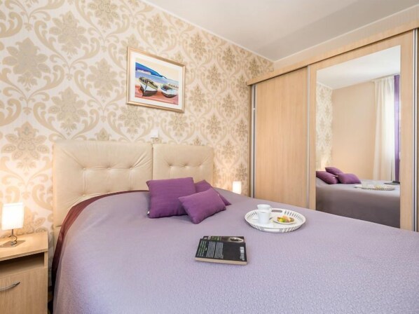 Et hotelværelse med en stor seng, et natbord med lampe, et bakke med morgenmad og et billede på væggen.