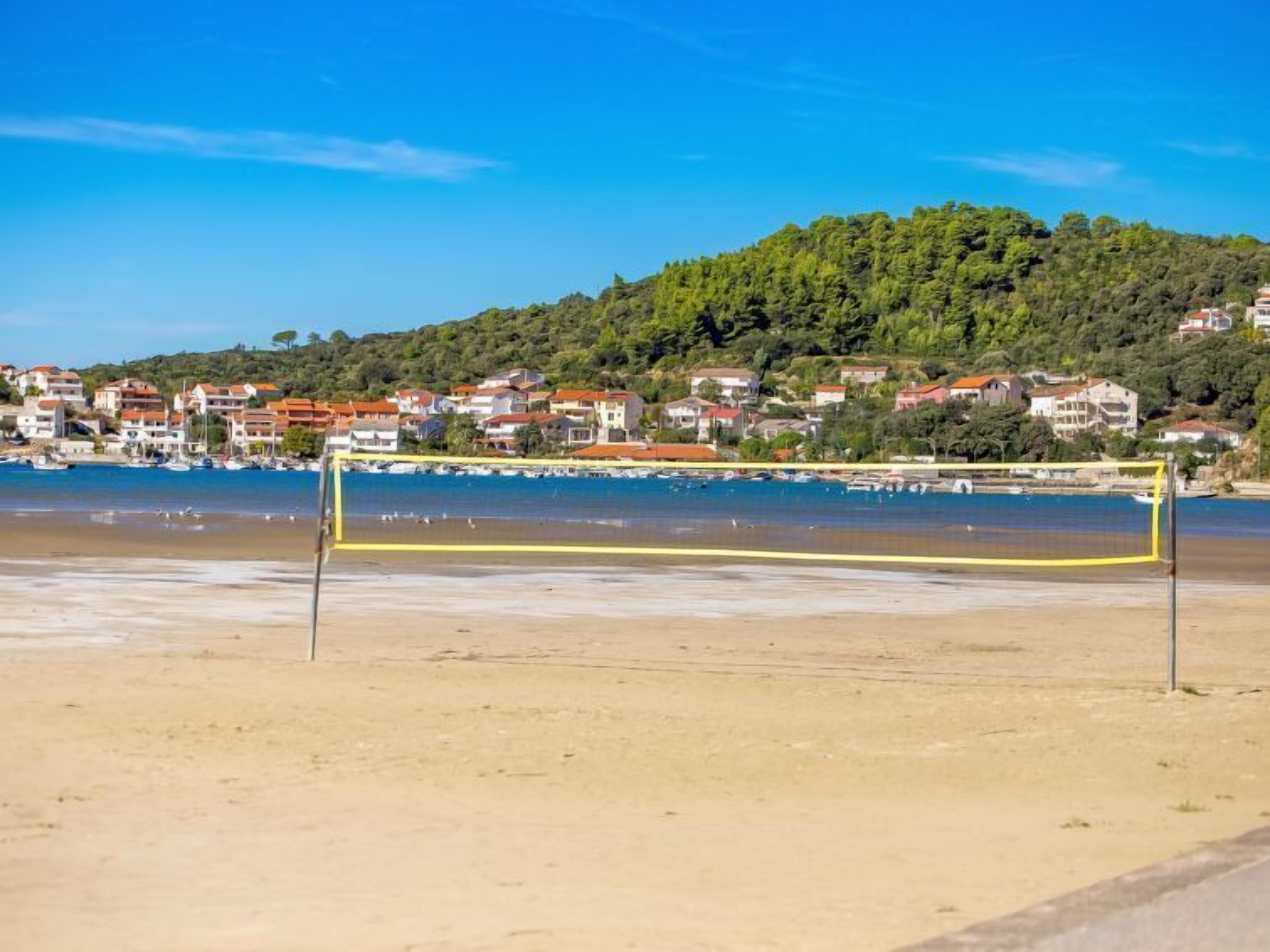 Een strandvolleybalnet op een zanderig strand, met op de achtergrond huizen en een heuvel.