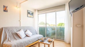 Een gezellige woonkamer met een grijze bank, een houten salontafel met lekkernijen, en een grote schuifpui die leidt naar een balkon.