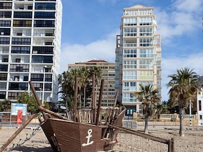 A beachfront hotel with multiple floors, palm trees, and a wooden boat structure.