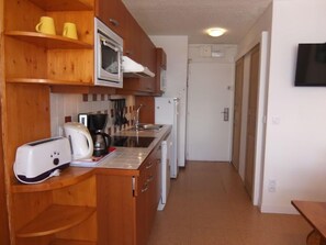 Una cocina compacta con armarios de madera, microondas, cafetera y tostadora.