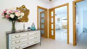 Un couloir avec une commode blanche, un miroir et un vase de fleurs.