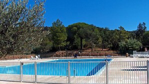 Ein Schwimmbecken mit einem Metallzaun, umgeben von einer Terrassenfläche mit Stühlen und einem Baum.
