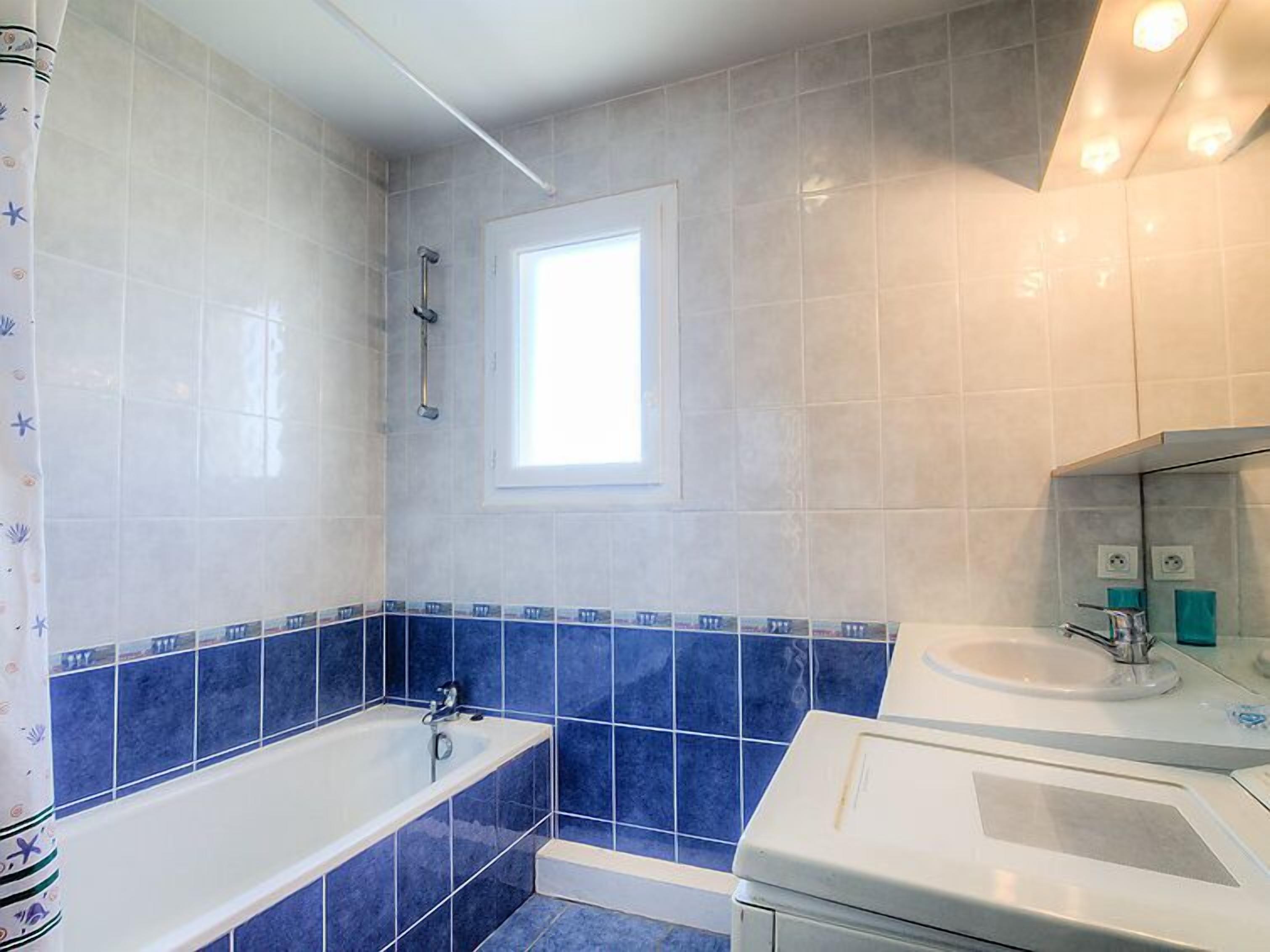 Een badkamer met een bad, een raam en een wastafel.