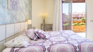 A bedroom with a bed, a nightstand, a lamp, a vase with flowers, and a view of the outside. - Duplex Bencomo by Interhome (Palm- Mar)