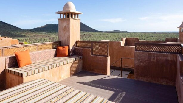 A rooftop terrace with a view of a mountain range, a seating area with cushions, and a decorative tower. - Duplex Bencomo by Interhome (Palm- Mar)