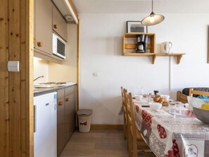 A compact kitchen with wooden cabinets, a microwave, a coffee maker, and a dining table set with a tablecloth.