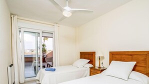 Quarto de hotel com duas camas, um ventilador de teto, mesa de cabeceira com abajur e uma porta de correr para área externa.