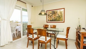Uma sala de jantar com mesa de vidro, cadeiras de madeira, luminária pendente e um quadro na parede.