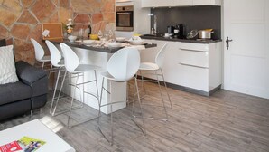A modern kitchen with white cabinetry, a stone accent wall, and a bar area with white chairs. - Apartment Stem 2 by Interhome (Verbier)