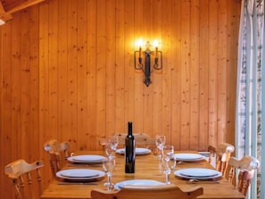 Een kamer met houten lambrisering, een eettafel gedekt voor zes personen, omringd door houten stoelen. Op de tafel staan een fles wijn en wijnglazen.