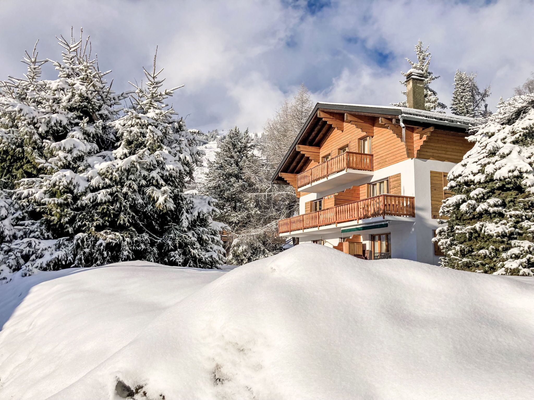 Una cabaña de madera de varios pisos con balcones, rodeada de árboles cubiertos de nieve.