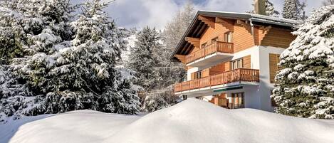 Una cabaña de madera de varios pisos con balcones, rodeada de árboles cubiertos de nieve.