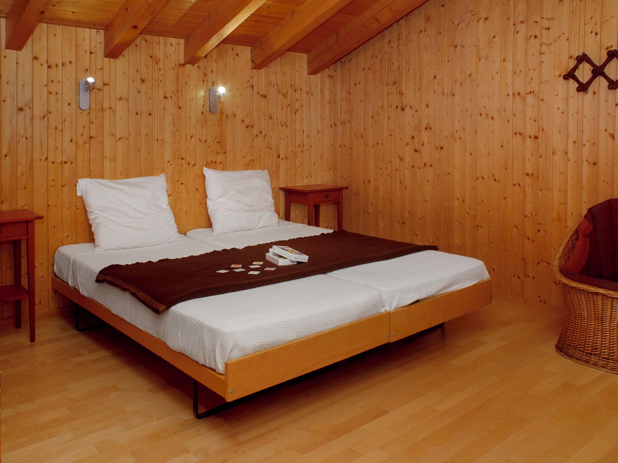 A wooden-paneled bedroom with a double bed, two bedside tables, and a wicker chair.