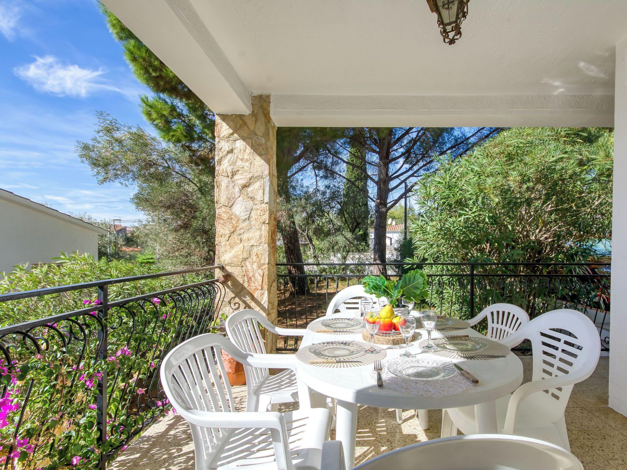 A covered outdoor dining area with a stone pillar, white plastic chairs, and a table set for two.