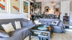 Un salon moderne avec un canapé gris, une table basse sur laquelle sont posés des magazines et un coin repas agrémenté d’un lustre.