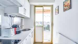 Une cuisine moderne avec des meubles blancs, une cuisinière et un évier. Une fenêtre offre une vue sur les bâtiments environnants.