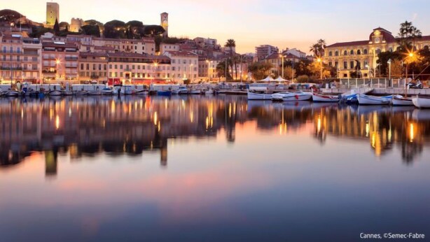 Une vue sur la ville, avec des bâtiments historiques le long du front de mer, un port de plaisance rempli de bateaux et un ciel dégagé.