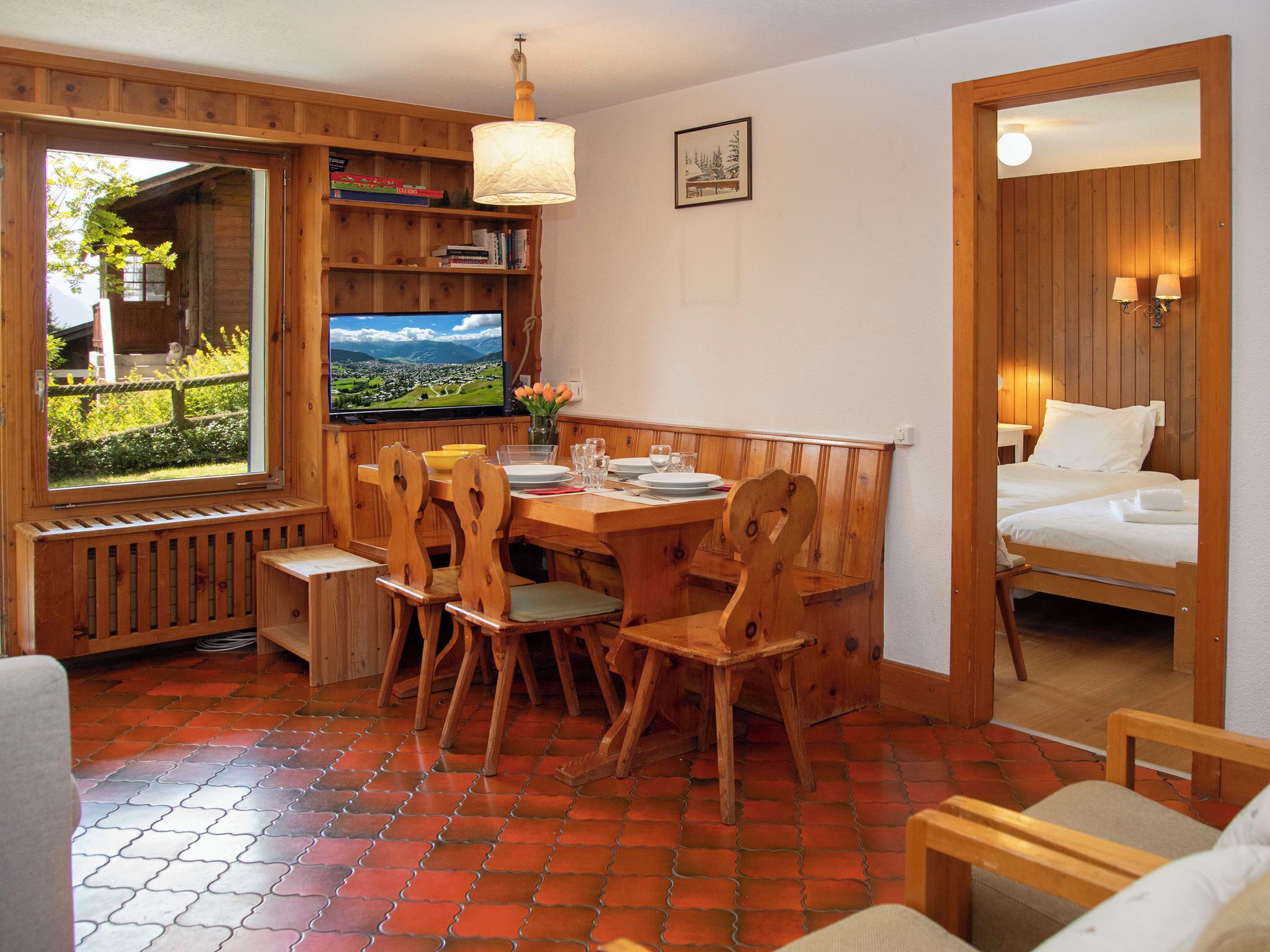 Une pièce chaleureuse avec une table à manger en bois, des chaises, un téléviseur et un lit.