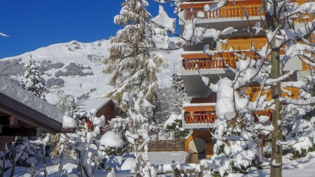 Un bâtiment enneigé, doté de nombreux balcons, avec une chaîne de montagnes en arrière-plan.
