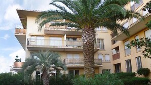 A multi-story hotel with balconies, palm trees, and a well-maintained garden.