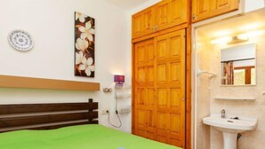 A hotel room with a green bed, wooden wardrobe, and a white sink. - Adelfa apt. 1 by Interhome (L'Escala)
