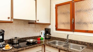A kitchen with white cabinets, granite countertops, a double sink, and a window with a textured glass door. - Adelfa apt. 1 by Interhome (L'Escala)