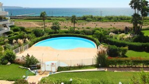 Ein Resort mit einem großen Swimmingpool, umgeben von üppiger Vegetation und Palmen, mit Blick auf einen Strand und den Ozean.