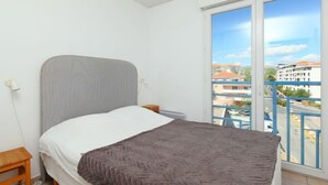 Ein Schlafzimmer mit Bett, Nachttisch, Fenster und Blick auf Gebäude und Straße.