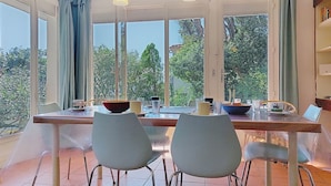 Ein Essbereich mit Tisch, Stühlen und großen Fenstern mit Blick auf Grünflächen.