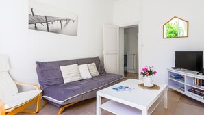 Een moderne woonkamer met een grijze bank, een witte salontafel, een witte fauteuil, een tv op een wit meubelstuk en een boekenkast.