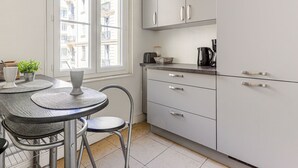 Een moderne keuken met witte kastjes, een ronde tafel met stoelen en een raam met uitzicht op gebouwen.