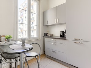 A modern kitchen with white cabinets, a round table with chairs, and a window with a view of buildings. - Apartment Hérold by Interhome (Nice)