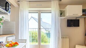 A modern kitchen with a microwave, a dining table with fruits, and a view of a house through a glass door. - Rose des Vents by Interhome (Quiberon)