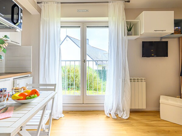 A modern kitchen with a microwave, a dining table with fruits, and a view of a house through a glass door.
