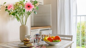 A dining table with a vase of flowers, a bowl of fruit, a coffee cup, and a dessert plate. - Rose des Vents by Interhome (Quiberon)