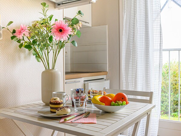 A dining table with a vase of flowers, a bowl of fruit, a coffee cup, and a dessert plate.
