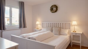 Une chambre à coucher comprenant un lit, deux tables de chevet, une fenêtre avec des rideaux, un radiateur et une couronne décorative accrochée au mur.