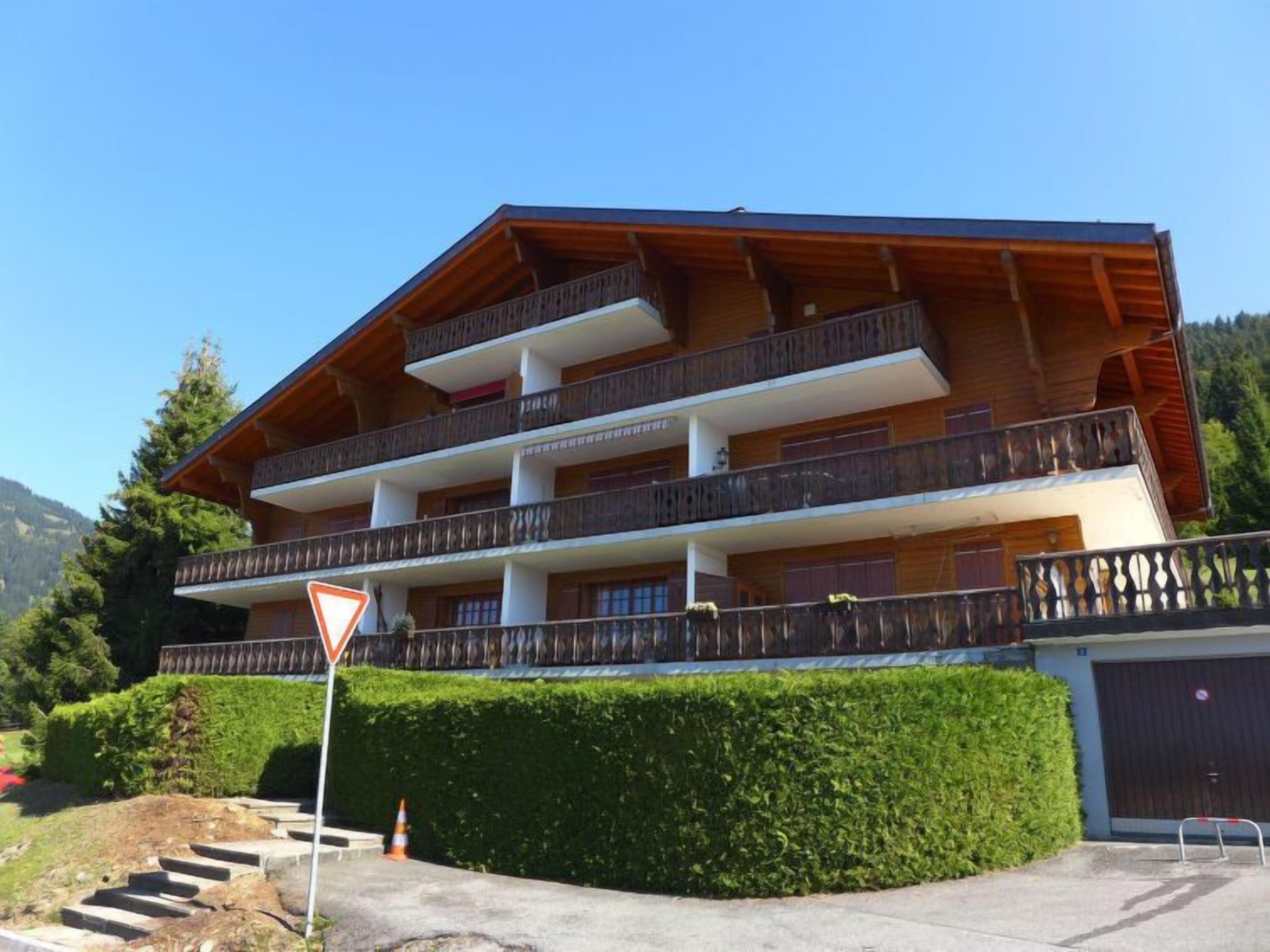 Un hotel de varios pisos con balcones, una señal que indica un giro a la derecha y montañas al fondo.