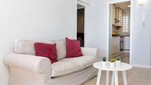 A living room with a beige sofa, red patterned pillows, and a small white table with potted plants. - Clipper by Interhome (Sant Vicenç de Montalt)