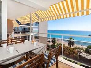 Un balcon avec une table et des chaises, donnant sur une plage et l’océan.