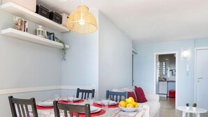 A dining area with a table set for four, chairs, a hanging light fixture, and a kitchen visible in the background. - Clipper by Interhome (Sant Vicenç de Montalt)